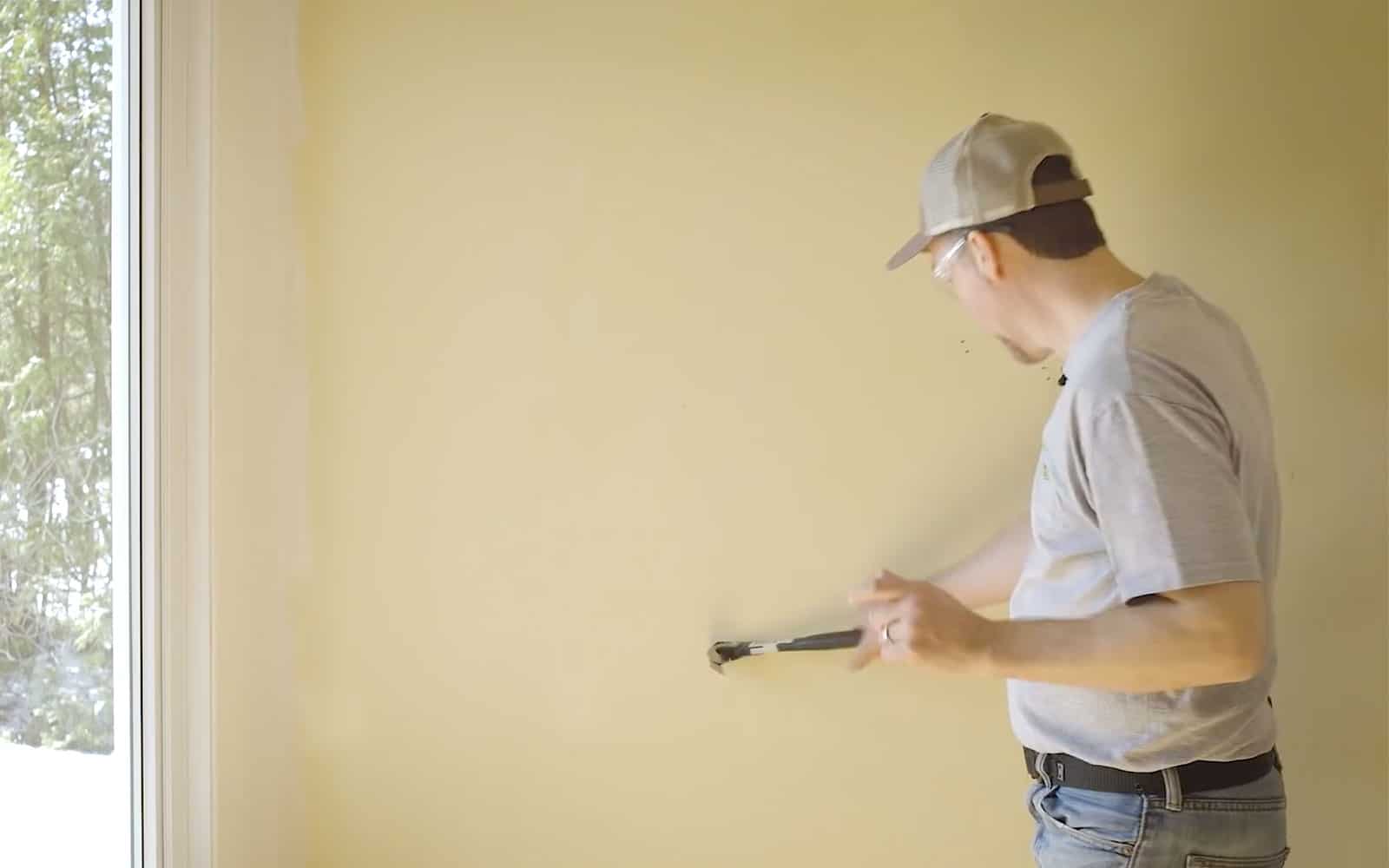 Synvain Rénove trou un mur avec un marteau
